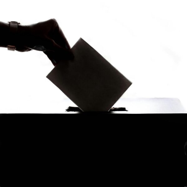 Silhouette of a hand placing a vote into a ballot box, symbolizing democracy.