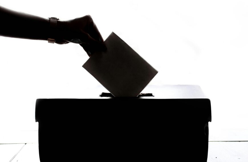 Silhouette of a hand placing a vote into a ballot box, symbolizing democracy.